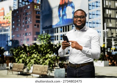 Black man checking apps on mobile phone during walk on downtown street, vibrant energy creating a strong personal presence within busy urbanistic setting near a park. City life.