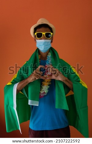 Black man in costume for carnival with brazil flag and pandemic mask isolated on orange background.
