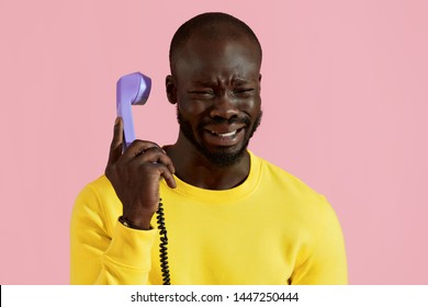 Black Man Crying, Talking On Phone On Pink Background. Portrait Of Upset African American Male With Sad Face Expression Calling On Purple Landline Phone In Studio