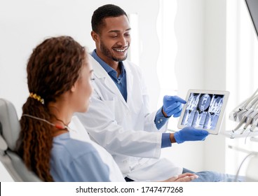 Black Man Dentist And Woman Patient Looking At Xray Picture On Digital Tablet At Clinic