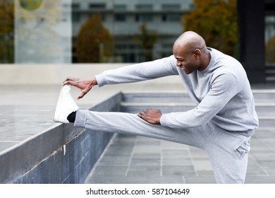 Black man doing stretching before running in urban background. Young male exercising