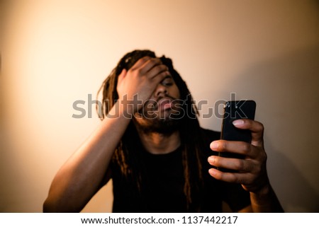 black man with dreadlocks in despair looking at phone