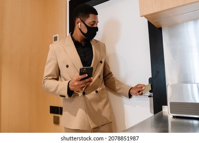 Black Man In Face Mask Using Cellphone While Opening Door At Hotel Indoors