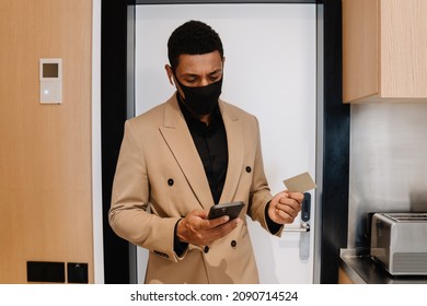 Black Man In Face Mask Using Cellphone While Opening Door At Hotel Indoors