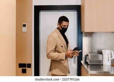 Black Man In Face Mask Using Cellphone While Opening Door At Hotel Indoors