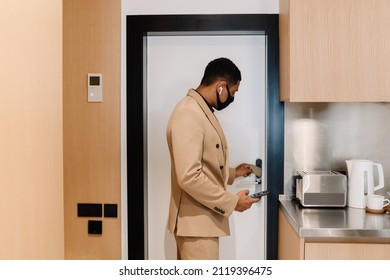 Black Man In Face Mask Using Cellphone While Opening Door At Hotel Indoors