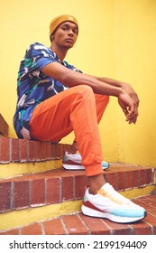 Black Man, Fashion And Street Style Clothes On Cool, Trend Or Attitude Model On Steps By City Wall Background On Building. Portrait Of Serious Student Sitting On Stairs In Urban Punk Clothing Outdoor