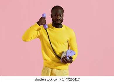 Black Man Having Unpleasant Phone Call On Pink Background. Portrait Of Male With Weird 