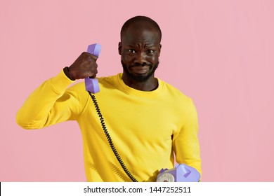 Black Man Having Unpleasant Phone Call On Pink Background. Portrait Of Male With Weird 