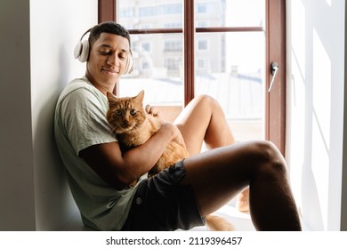 Black Man In Headphones Sitting With His Cat On Windowsill In Hotel