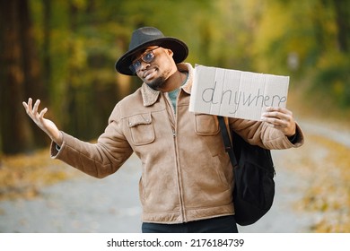 Black man hitchhiking on a road and holding a cardboard sign anywhere
