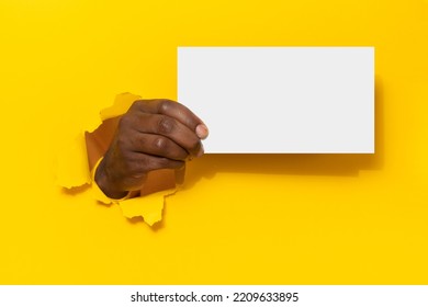 Black Man Holding Blank Placard White Sheet Through Hole In Yellow Paper Background, Presenting Empty Space For Your Design Or Text, Mockup