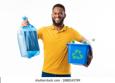 Black Man Holding Box With Recycling Plastic Litter And Blue Garbage Bag Standing On White Studio Background, Smiling To Camera. Waste Sorting And Recycling Concept