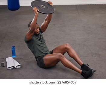 Black man holding weight plate for fitness, exercise and workout in gym. Strong bodybuilder weightlifting on floor for power, energy and heavy sports challenge in training, muscle gain and balance