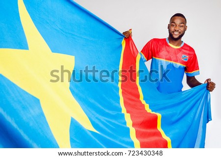 A black man holds the flag of the Democratic Republic of the Congo. The man is African.