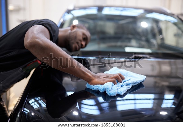 black man holds the\
microfiber in hand and polishes the car in auto service, do it\
carefully after repair
