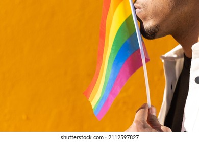 Black Man Kissing A Rainbow Lgtb Flag Next To A Yellow Wall On The Background