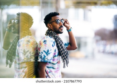 Black Man Leaning Against A Glass Wall Holding His Sunglasses