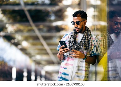 Black Man Leaning Against A Glass Wall Using His Smartphone