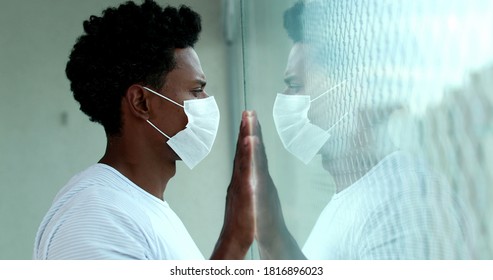 Black Man In Lockdown Wearing Covid-19 Mask Looking Out Apartment Window, African Person During Quarantine