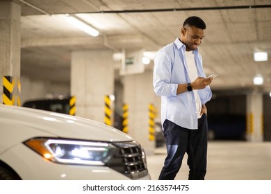 Black Man Looking At The Phone At His Car In The Parking Lot