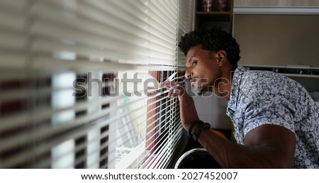 Black man looking through kitchen blinders looking outside