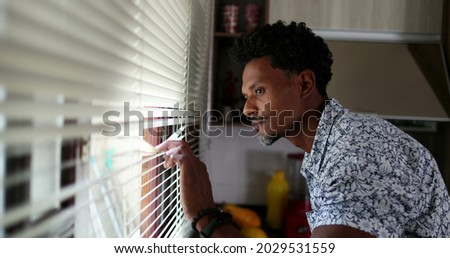 Black man looking through kitchen blinders looking outside