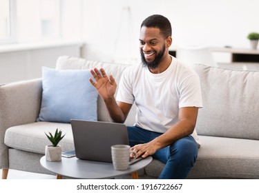 Black Man Making Video Call At Laptop Talking With Distant Family, Waving Hello To Computer Webcam Sitting On Sofa At Home. Remote Online Communication Concept