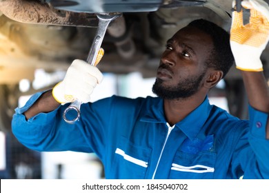 Black man mechanic working Under a Vehicle in a Car Service station. Expertise mechanic working in automobile repair garage. 