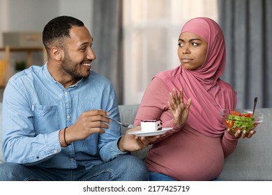 Black Man Offering Cake To His Pregnant Muslim Wife While She Eating Salad, Serious Islamic Lady In Hijab Refusing Sweets, Choosing Vegetables Over Dessert, Having Healthy Nutrition During Pregnancy