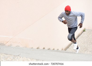 Black Man Running Upstairs Outdoors. Young Male Exercising With City Scape At The Background.