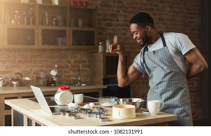 Black man seasoning food at home kitchen. African-american guy in apron baking cookies, adding flaworings to dough and having fun