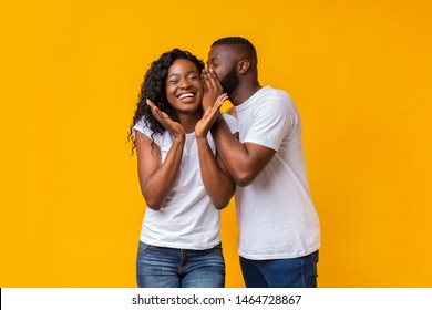 Black Man Sharing Secret With His Woman, girl is laughing, yellow studio background