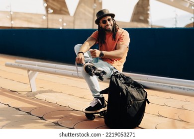 Black Man Sitting On The Bench. Modern Man Posing With Roller Skates.