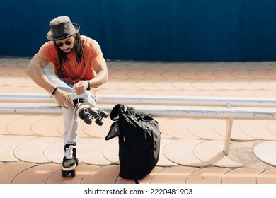 Black Man Sitting On The Bench. Modern Man Posing With Roller Skates.