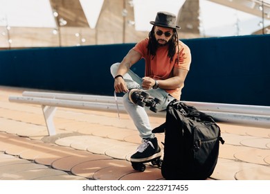 Black Man Sitting On The Bench. Modern Man Posing With Roller Skates.