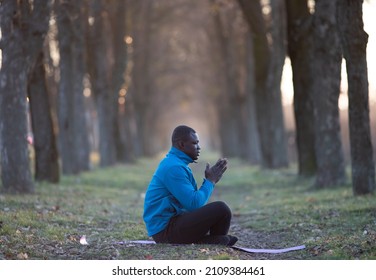 Black man sitting on exercising man in asana and meditating after workout outdoors in winter time