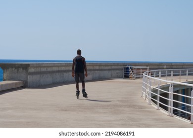 Black Man Skating On Roller Skates  Along The Promenade By The Sea On A Sunny Day.