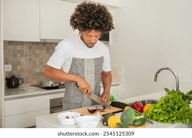 A black man is skillfully chopping vegetables on a wooden cutting board in a well-lit kitchen, surrounded by fresh produce. He is focused on preparing a healthy meal. - Powered by Shutterstock