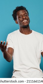 Black Man Speaking To Camera And Doing Hand Gestures In Studio. African American Person Talking And Looking At Camera. Casual Adult Making Presentation Speech And Smiling.