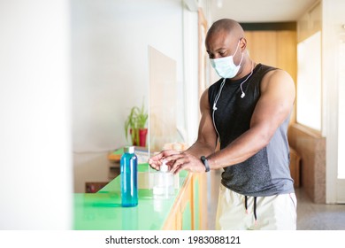 Black Man In Sportswear And Face Mask Spraying Sanitizing Gel On His Hands. He Is Entering The Gym.