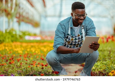 Black Man Squat And Holding A Digital Tablet In A Garden Center.