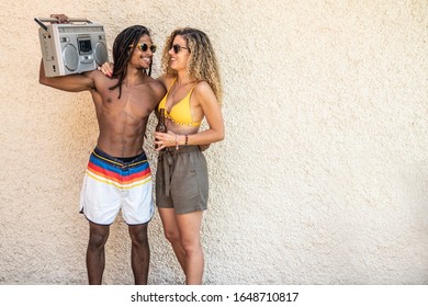 Black Man With A Stereo In His Hands Hugging A White Woman In A Bathing Suit