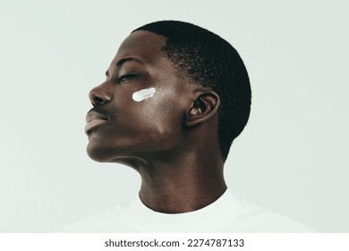 Black man taking care of his skin with a routine, he applies face cream to keep it moisturized and glowing. With his eyes closed, he enjoys the refreshing feeling of the beauty product on his skin. - Powered by Shutterstock