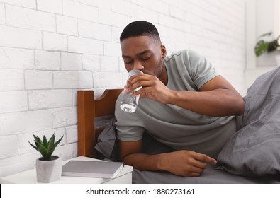Black Man Taking Glass Of Water Lying In Bed, Hydrating Drinking In Bedroom At Home In The Morning, Starting New Day With Fresh Aqua. Stay Hydrated. Healthy Liquid Concept. Selective Focus