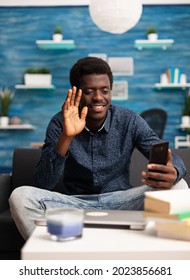 Black Man Talking On Online Video Call Conference In Bright Living Room, Using Smartphone Technology. African American Internet Online User Working From Home For Office Project Planning