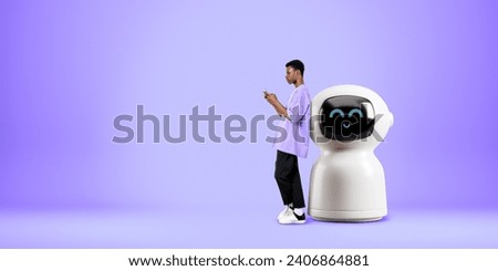 Black man typing in smartphone, standing full length near cartoon AI robot on copy space empty purple background. Concept of virtual assistant and artificial intelligence