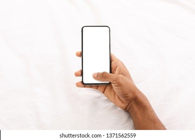 Black man using cellphone with blank screen in bed, mockup for app, pov
