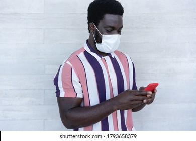 Black Man Using Mobile Phone - African Guy Wearing Face Protective Mask While Watching Video On Smartphone - Coronavirus Lifestyle And Fashion Concept - Focus On Face