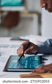 Black man using stylus interacting with digital tablet displaying data charts and analytics, close up of hand and device on desk, adult engaged in technology related task